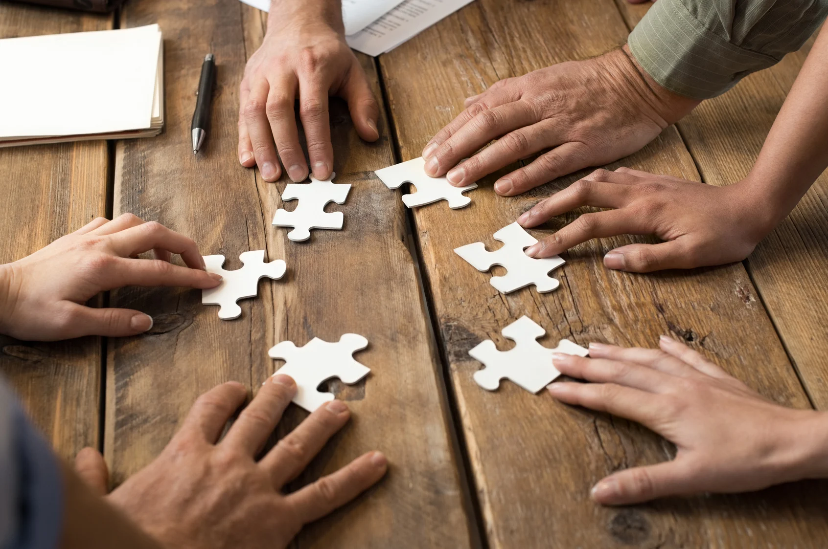 Mehrere Hände legen Puzzleteile auf einem Holztisch zusammen